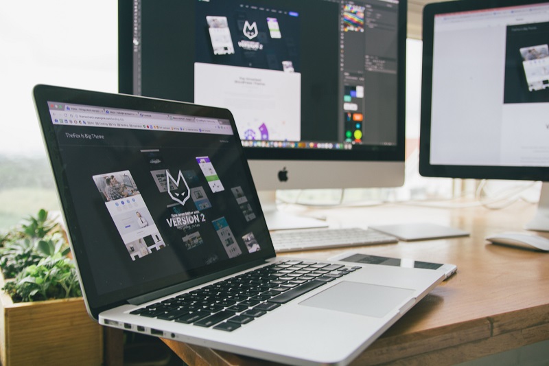 Web designer using a laptop and desktop monitors to create website layouts for a custom WordPress page template.