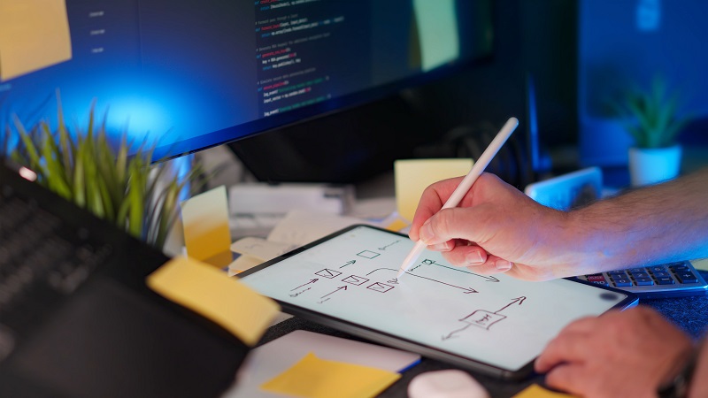 Editing a WordPress template with a digital tablet showing a website layout diagram beside a computer monitor.